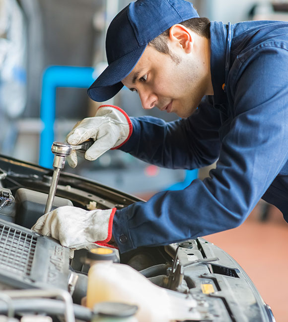mechanic in an auto service center standing over a car working on it