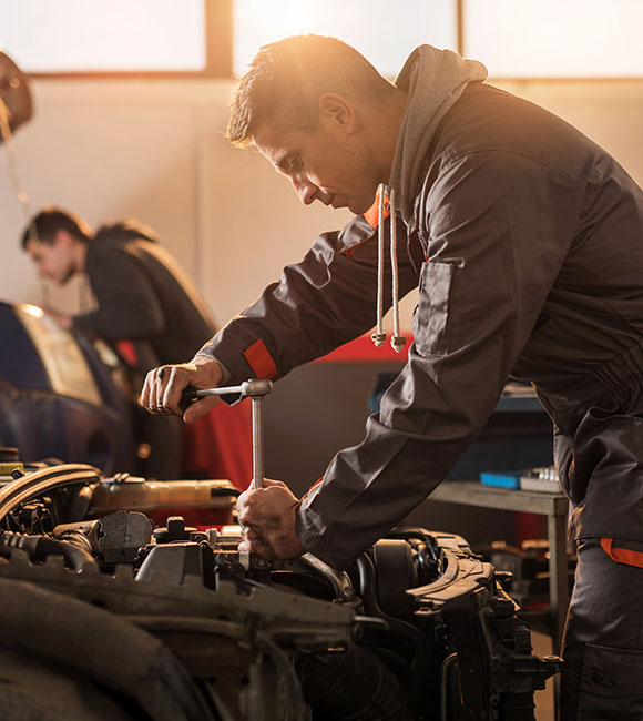 mechanic in an auto service center standing over a car working on it