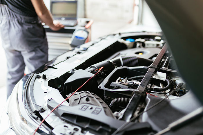 closeup of car with car hood up, mechanic stands in the background